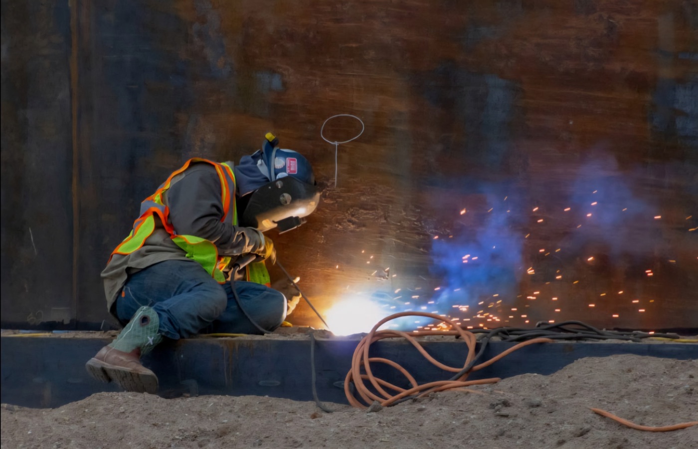 Welder wearing a hardhat and high-visibility vest during fabrication work